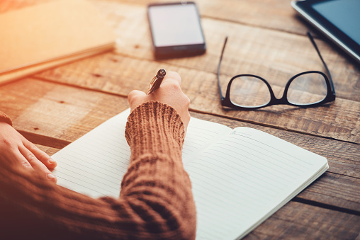 person in jumper writing on wooden desk